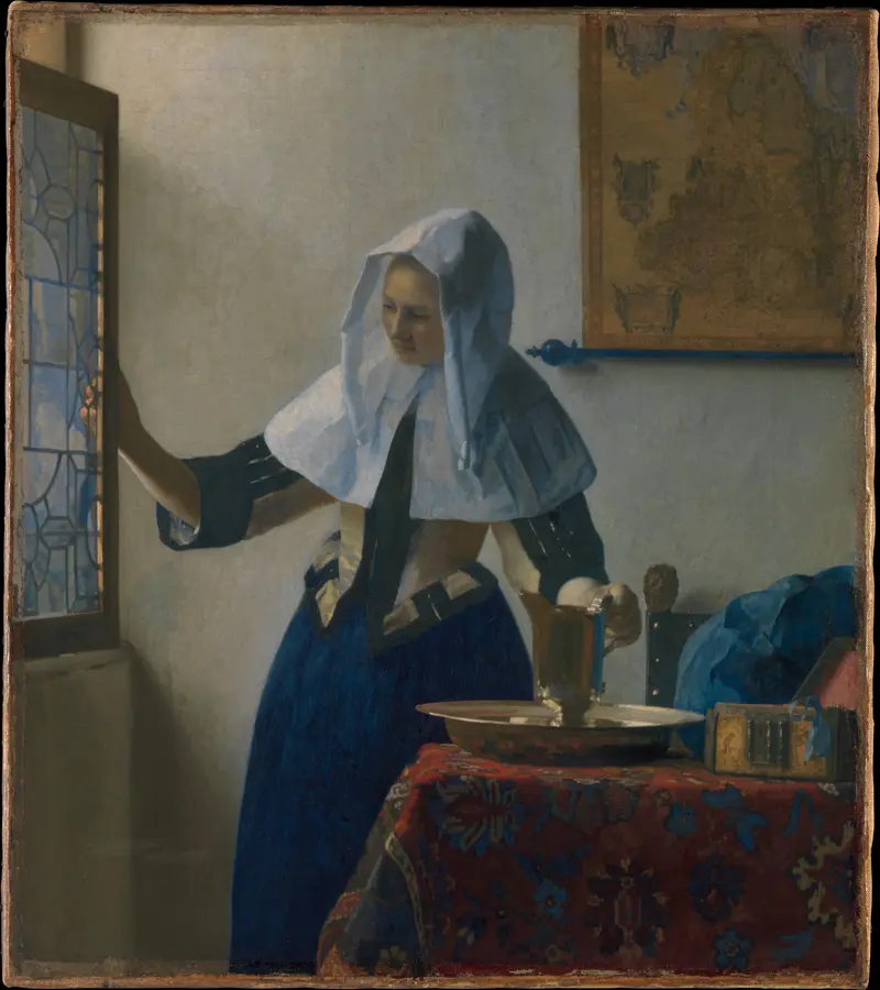 A young woman opens a leaded glass window with one hand while resting her other hand on a water pitcher on a table covered with a red patterned carpet.