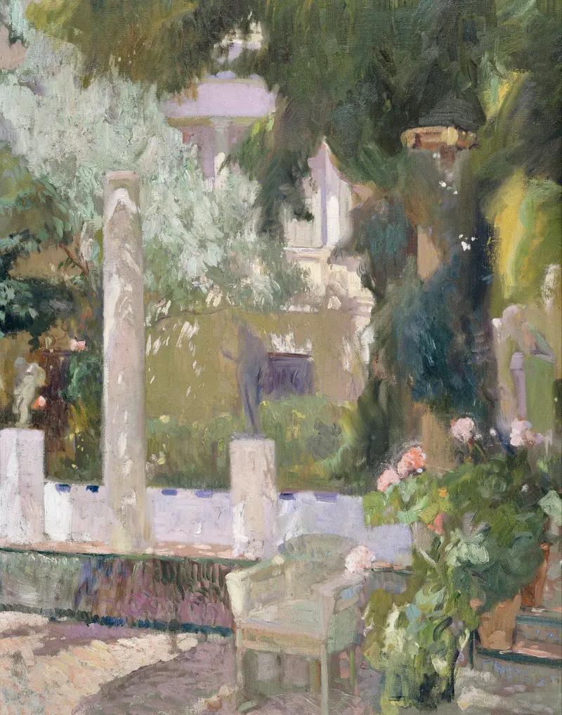A sunlit garden scene showing a wicker armchair, flowering shrubs, a low white wall with columns, and the pale facade of a house behind dense foliage.