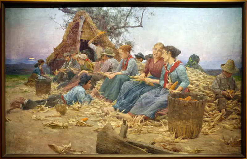 A group of women and men husking corn in a circle at dusk, surrounded by baskets and husks, with a soft light illuminating the scene.