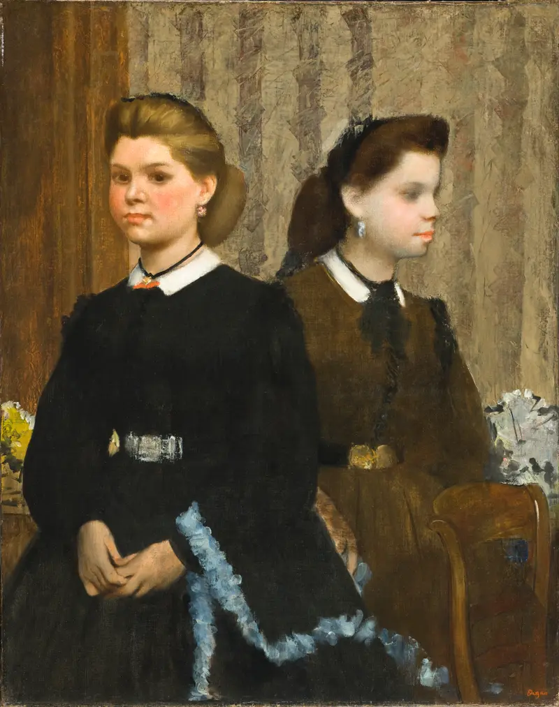 Two young girls, one seated in a black dress with pale blue ruffles and the other standing in a brown dress, posed side by side against patterned wallpaper.