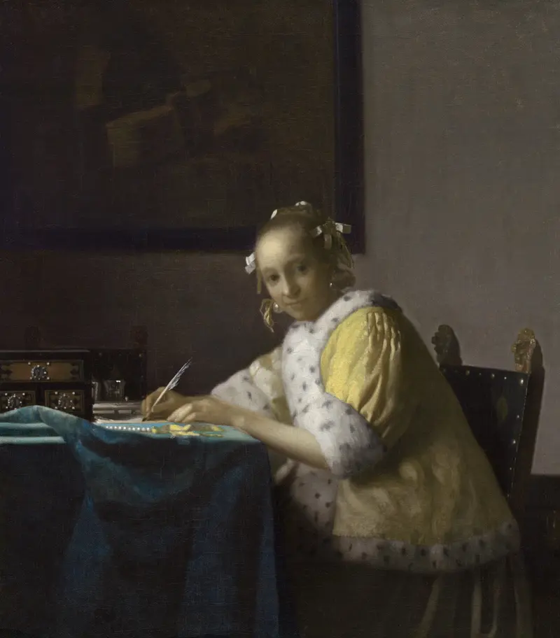 A young woman in a lemon-yellow jacket sits at a table writing a letter, with a string of pearls and papers nearby and a dark painting behind her.