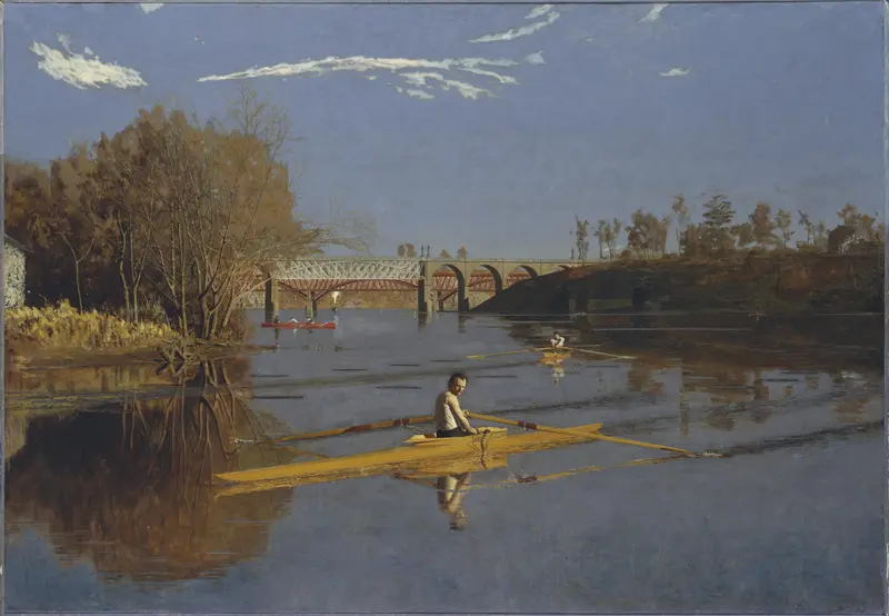 A lone rower in a yellow scull sits on a calm river with two other scullers and two bridges visible in the background under a clear sky.