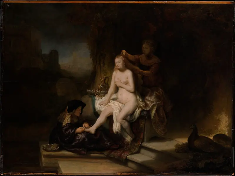 A nude woman sits illuminated by golden light while two attendants wash her foot and arrange her hair against a dark background.