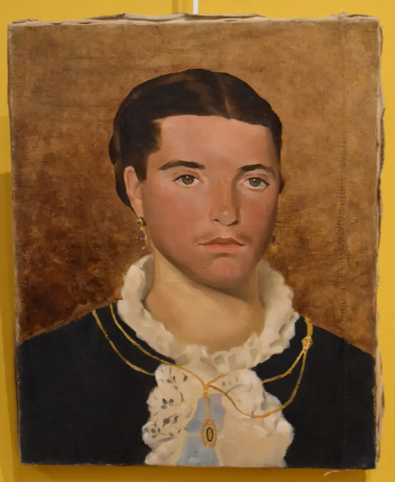 A woman gazes directly at the viewer, her lace collar and gold jewelry contrasting against a warm brown background.