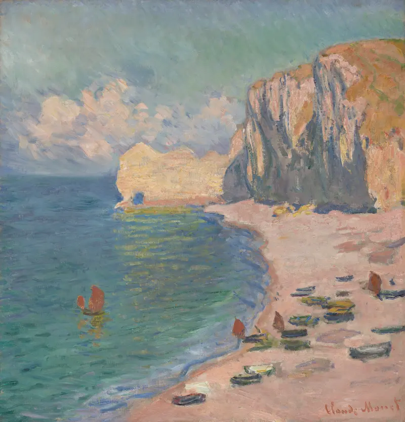 A curving beach bordered by steep cliffs with small boats scattered along the sand and water under a cloudy sky.