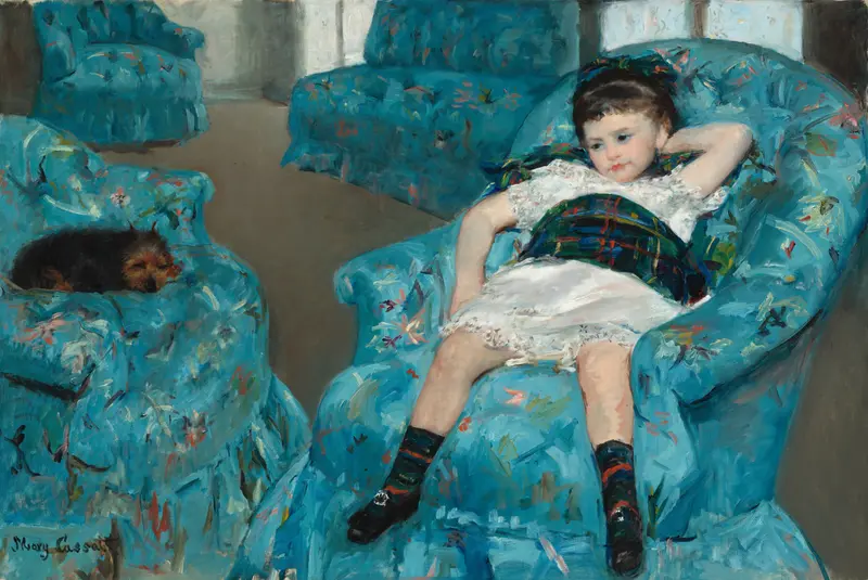 A young girl in a white dress reclines in a large blue armchair with a small dark-coated dog curled up on another blue armchair beside her.