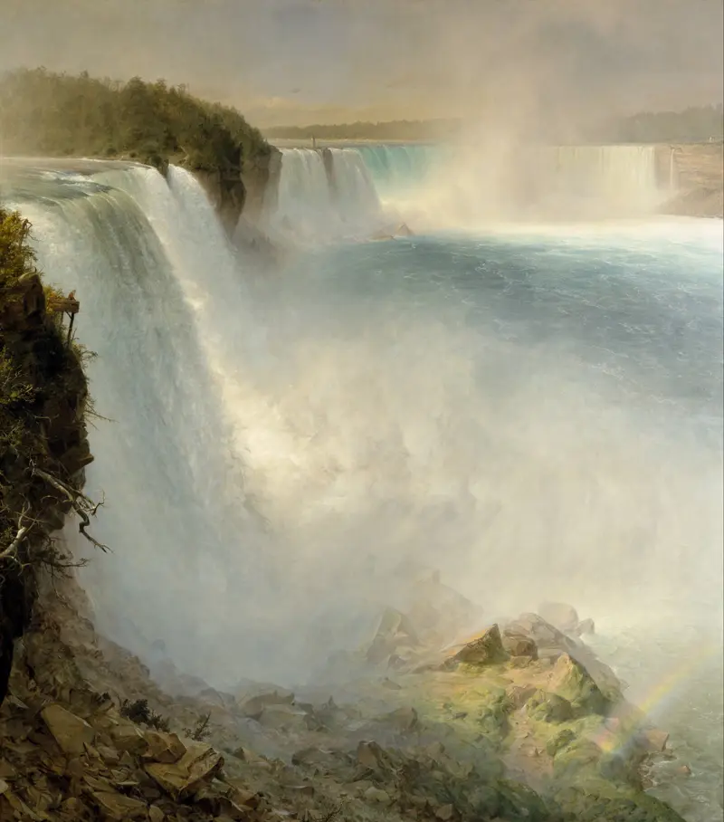 A view of Niagara Falls from the American side showing sheets of water plunging over a rocky cliff with mist, spray, a faint rainbow, and surrounding rocks and trees.