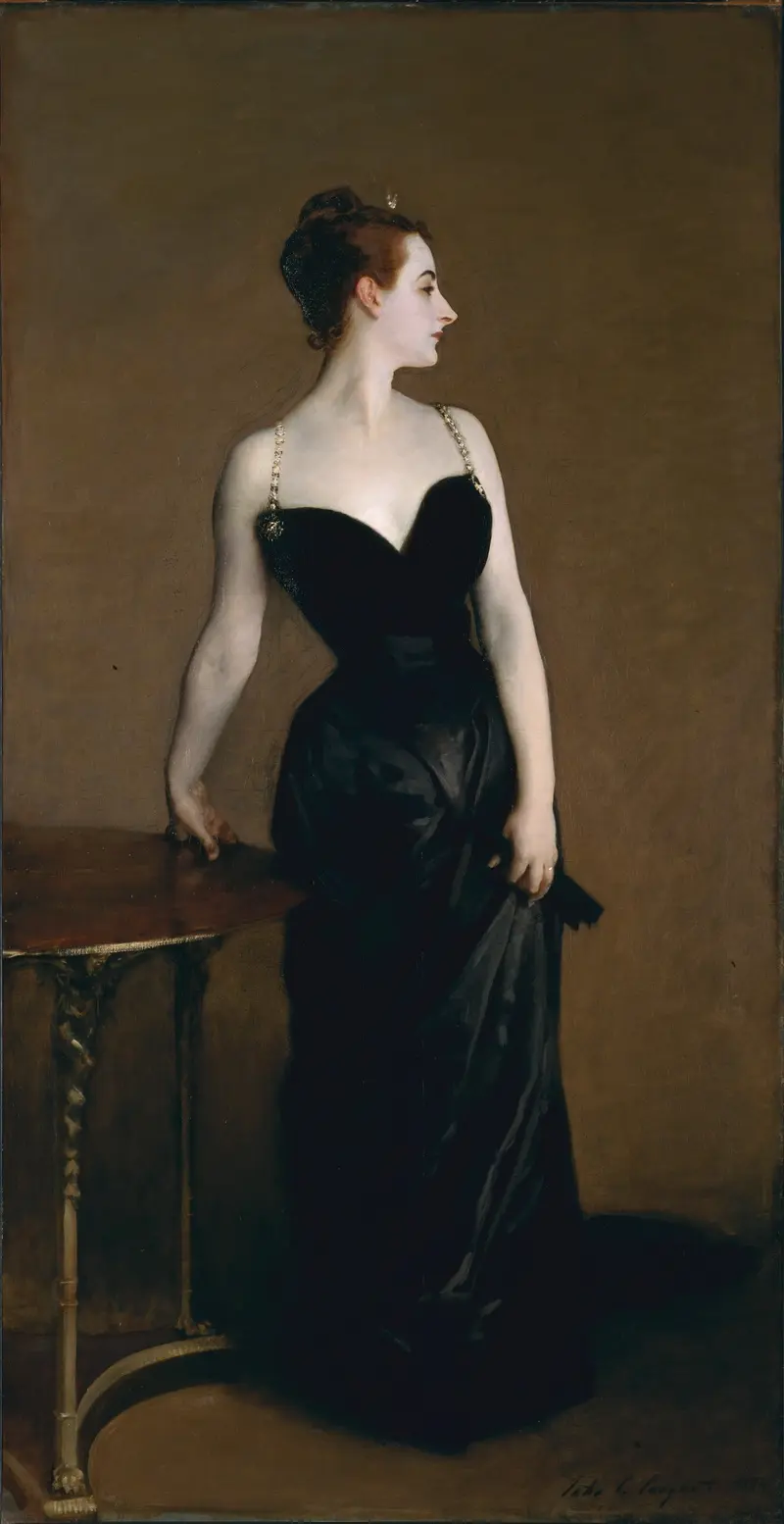 A woman in a black evening dress stands in profile beside a polished wooden table against a warm brown background.