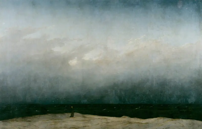 A solitary monk in a dark robe stands on a sandy shore facing a wide, dark sea beneath a vast, cloudy sky.