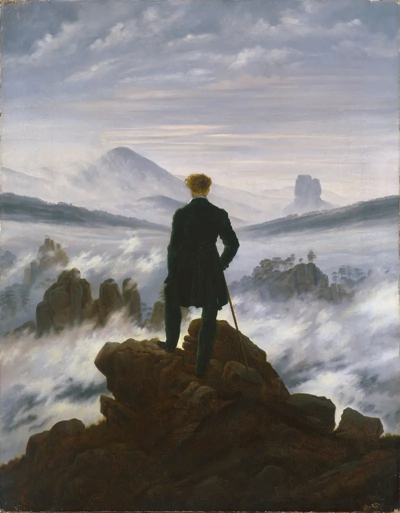 A solitary man in a green coat stands on a rocky outcrop, facing fog-covered mountains and valleys under a cloudy sky.